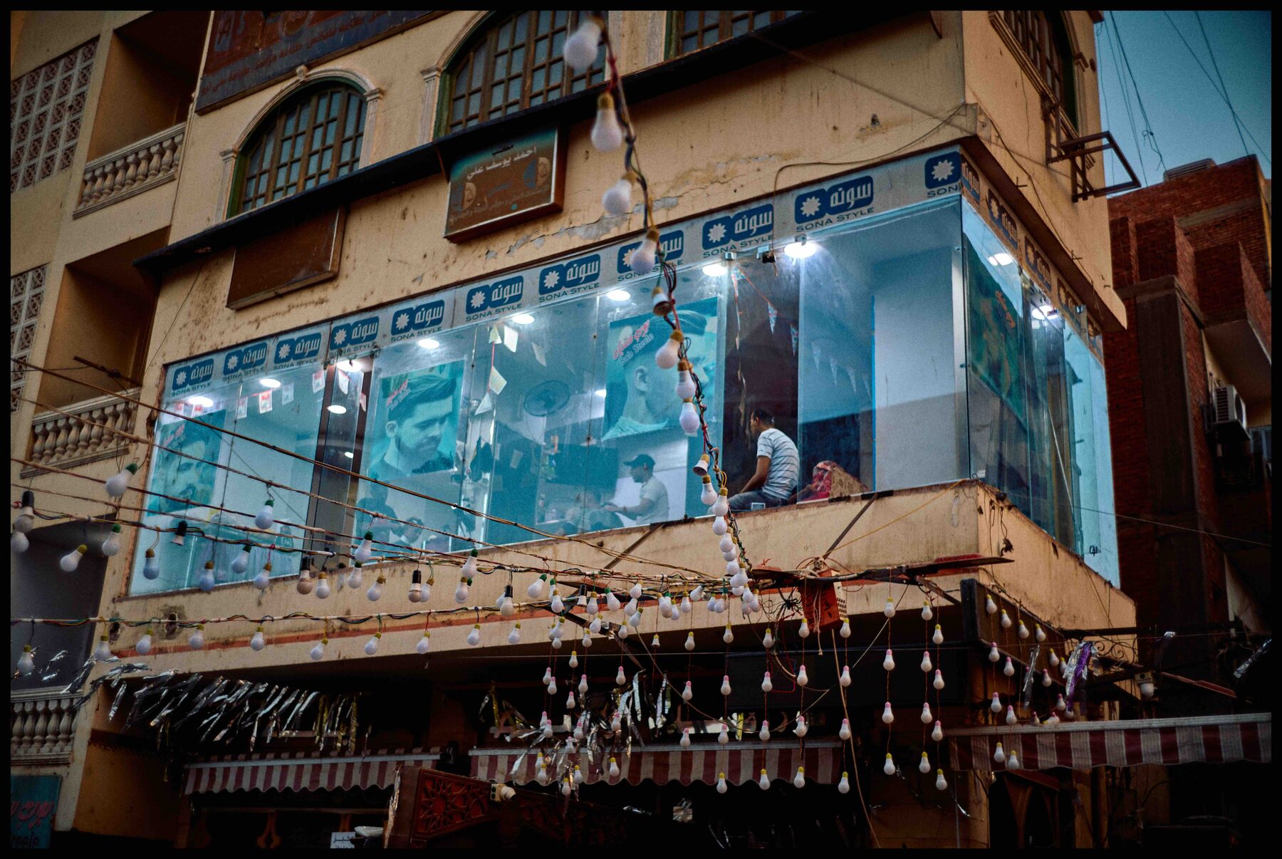 Aswan – Friseursalon hinter Glas, davor Glühbirnen-Girlanden