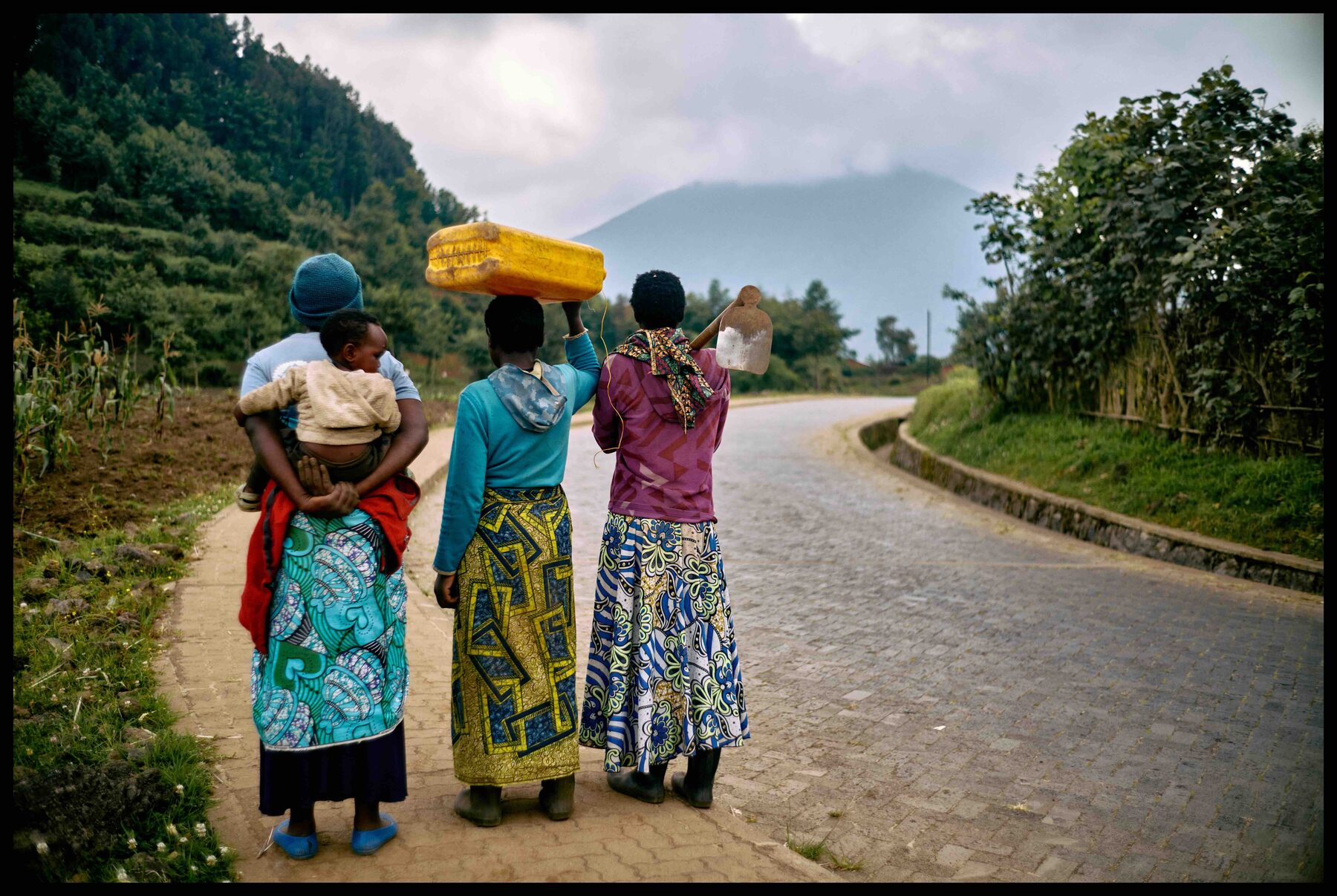 Ruanda – drei Frauen auf einer Straße, eine trägt einen Kanister auf dem Kopf
