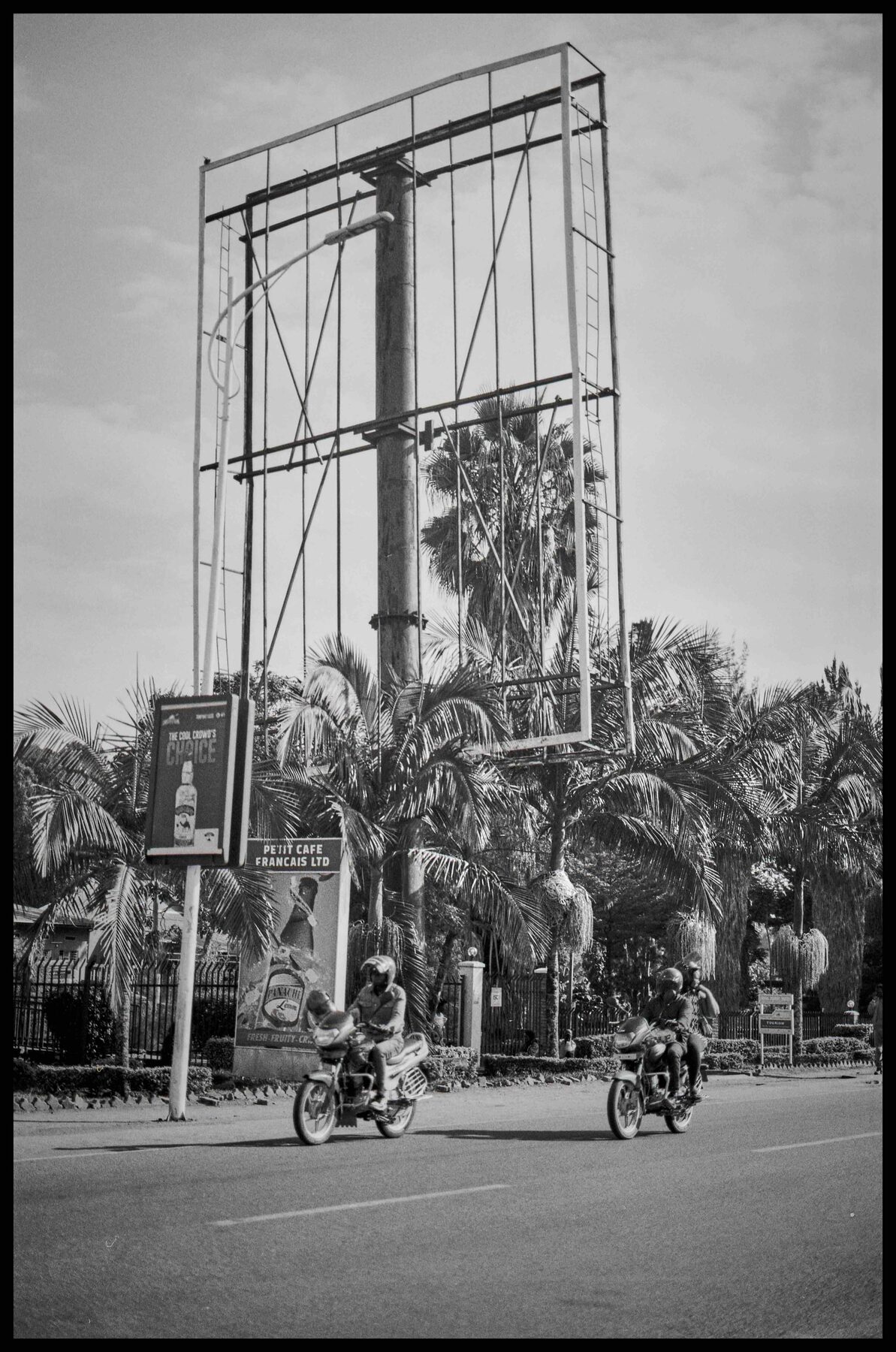Ruanda – Reklametafel an einer Straße mit Palmen und Motorrädern